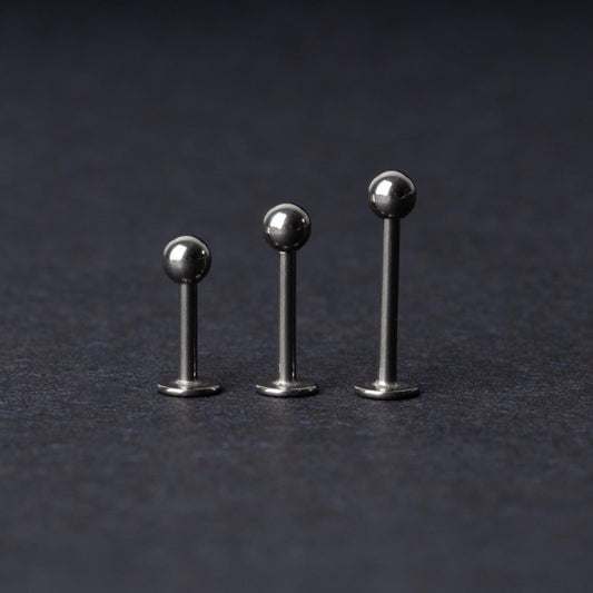 Three silver stainless steel labret studs with flat backs and polished ball ends, displayed on a dark textured background.