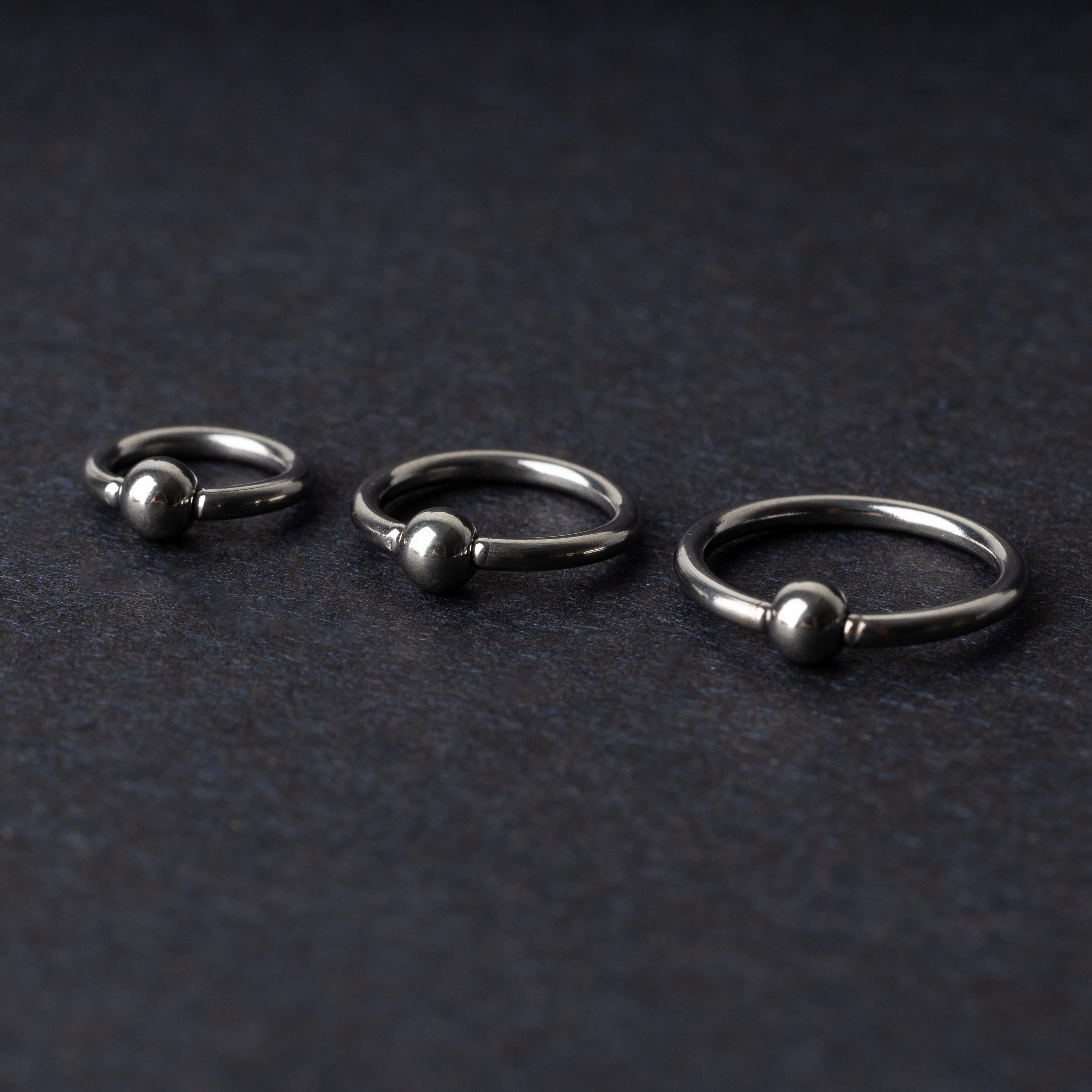 Three polished stainless steel captive bead rings of varying sizes displayed on a dark matte background.