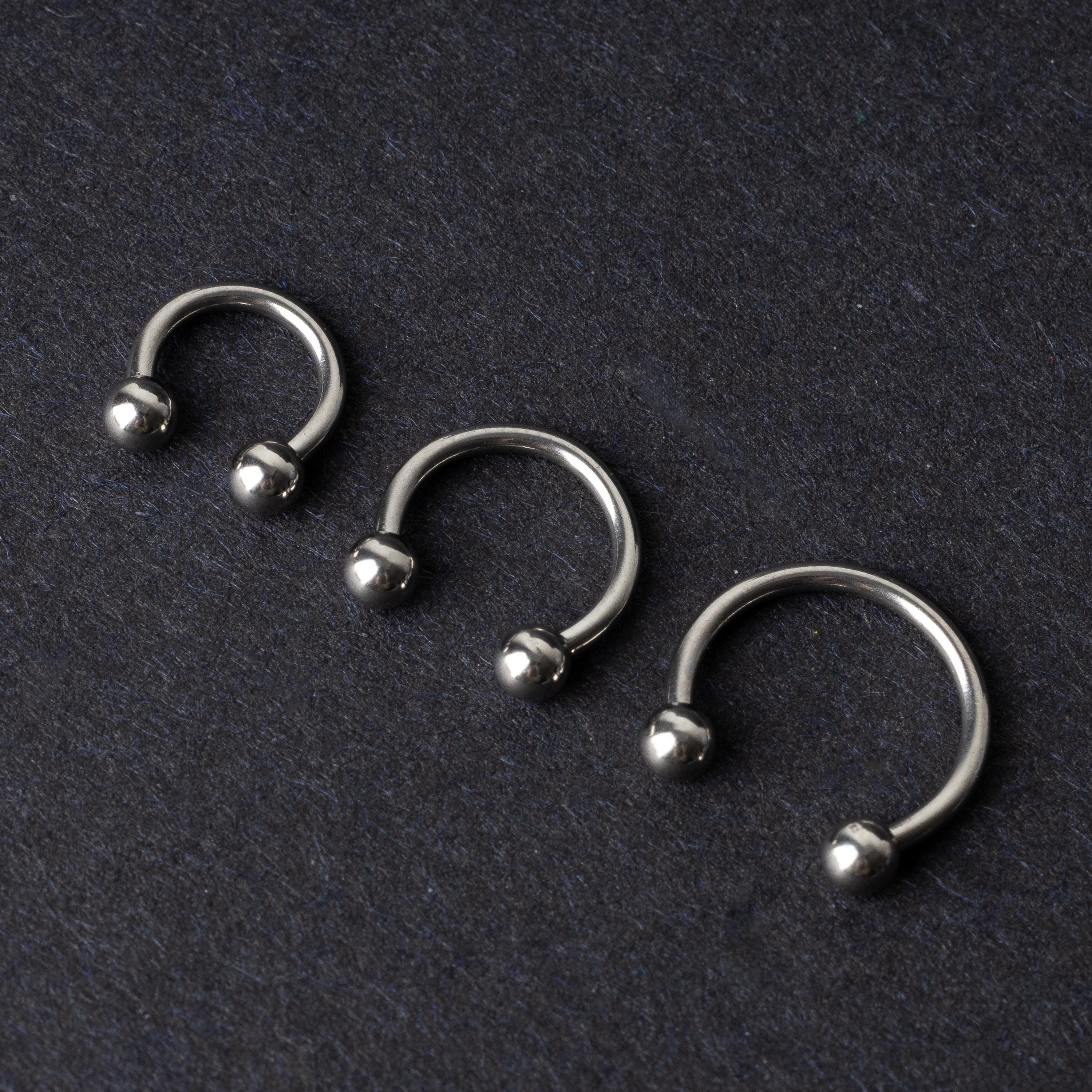 Three silver stainless steel horseshoe hoops with polished ball ends, displayed on a dark textured background.
