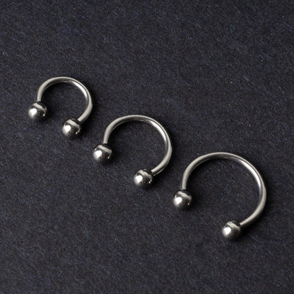 Three silver stainless steel horseshoe hoops with polished ball ends, displayed on a dark textured background.