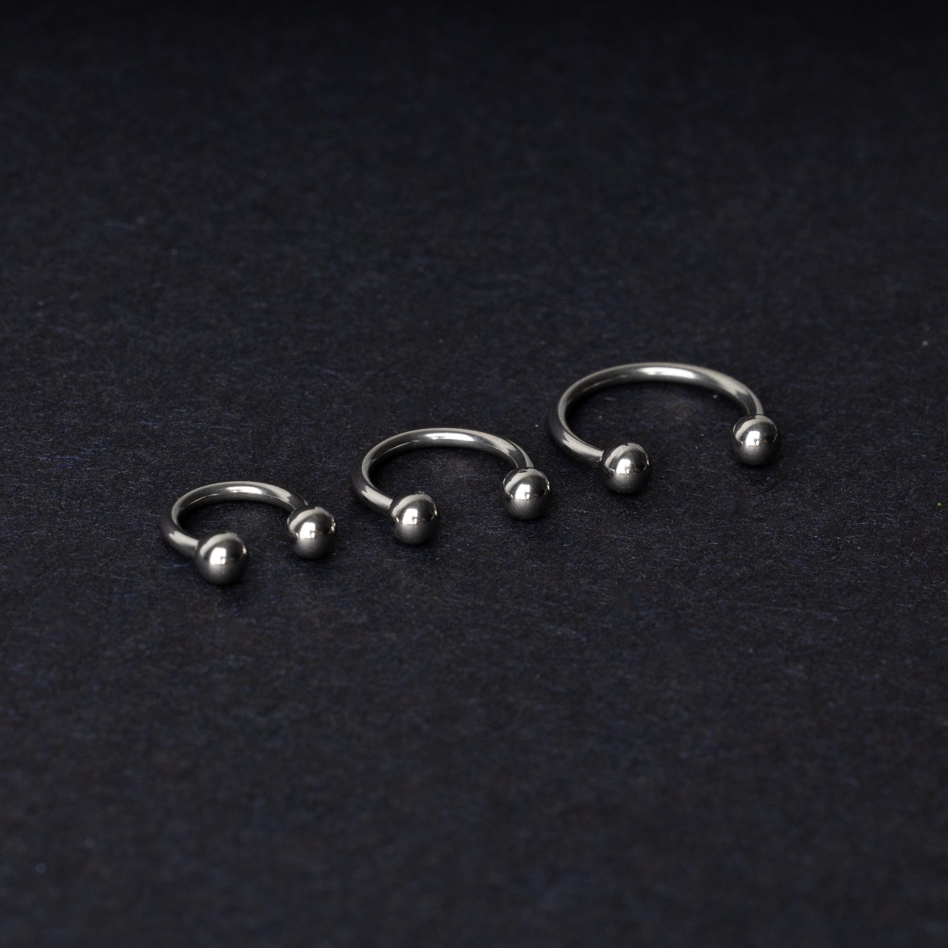 Three silver stainless steel horseshoe hoops with polished ball ends, displayed on a dark textured background.