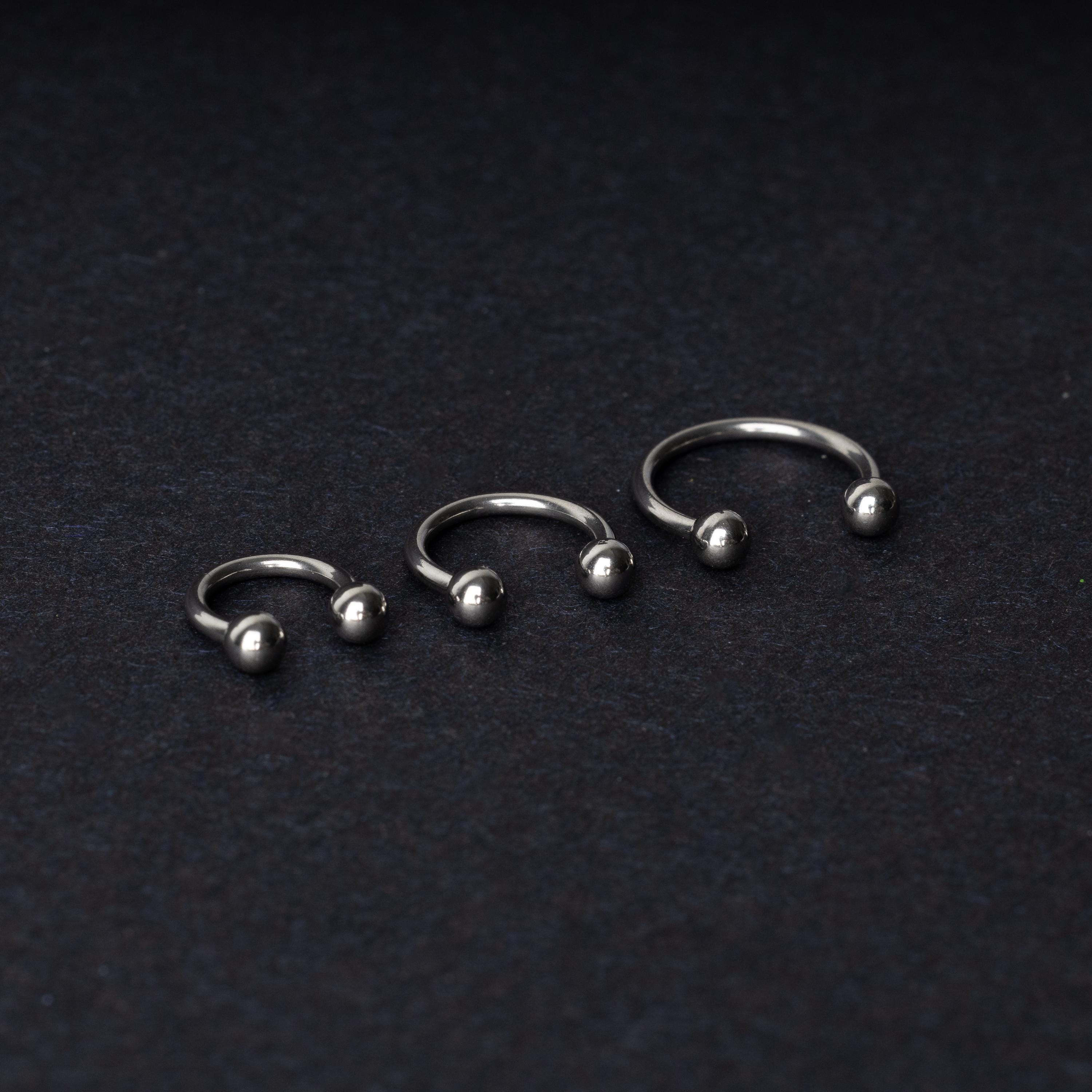 Three silver stainless steel horseshoe hoops with polished ball ends, displayed on a dark textured background.