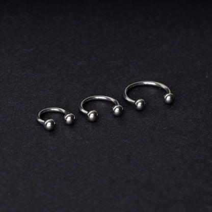 Three silver stainless steel horseshoe hoops with polished ball ends, displayed on a dark textured background.
