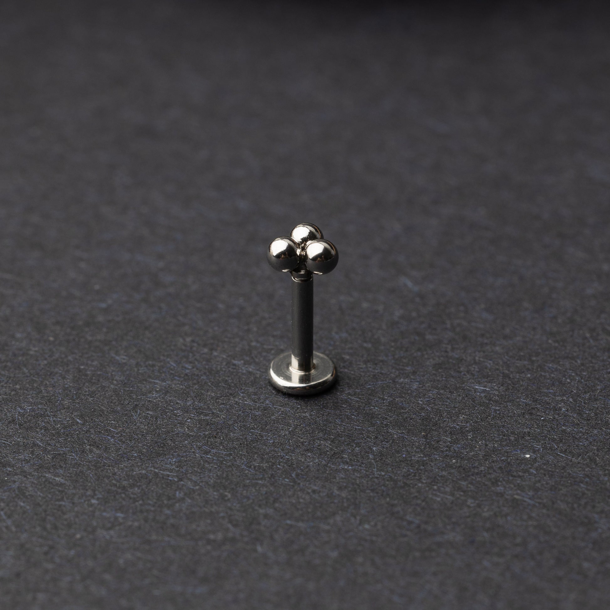 Close-up of three minimalist ball cluster labret studs in a silver finish, displayed on a dark background.
