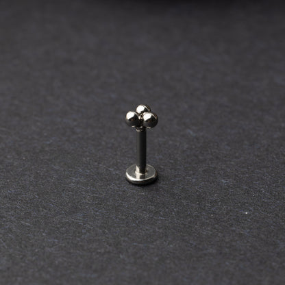 Close-up of three minimalist ball cluster labret studs in a silver finish, displayed on a dark background.
