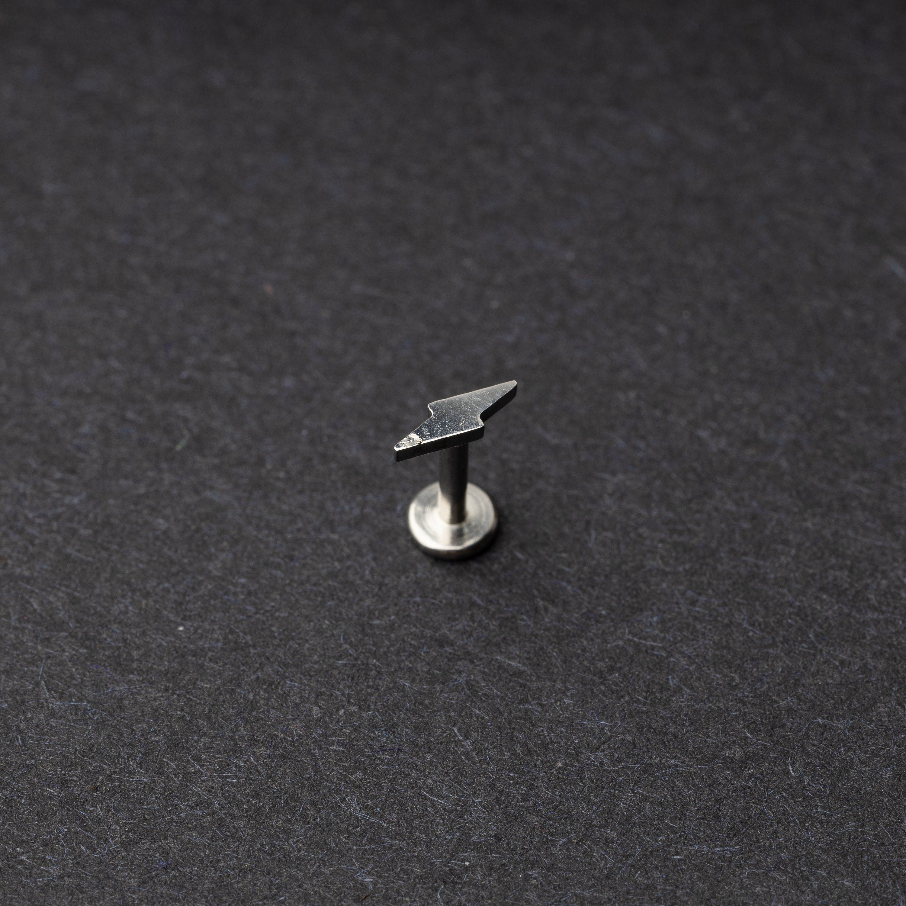 Minimalist lightning bolt labret studs in silver displayed on a dark background.