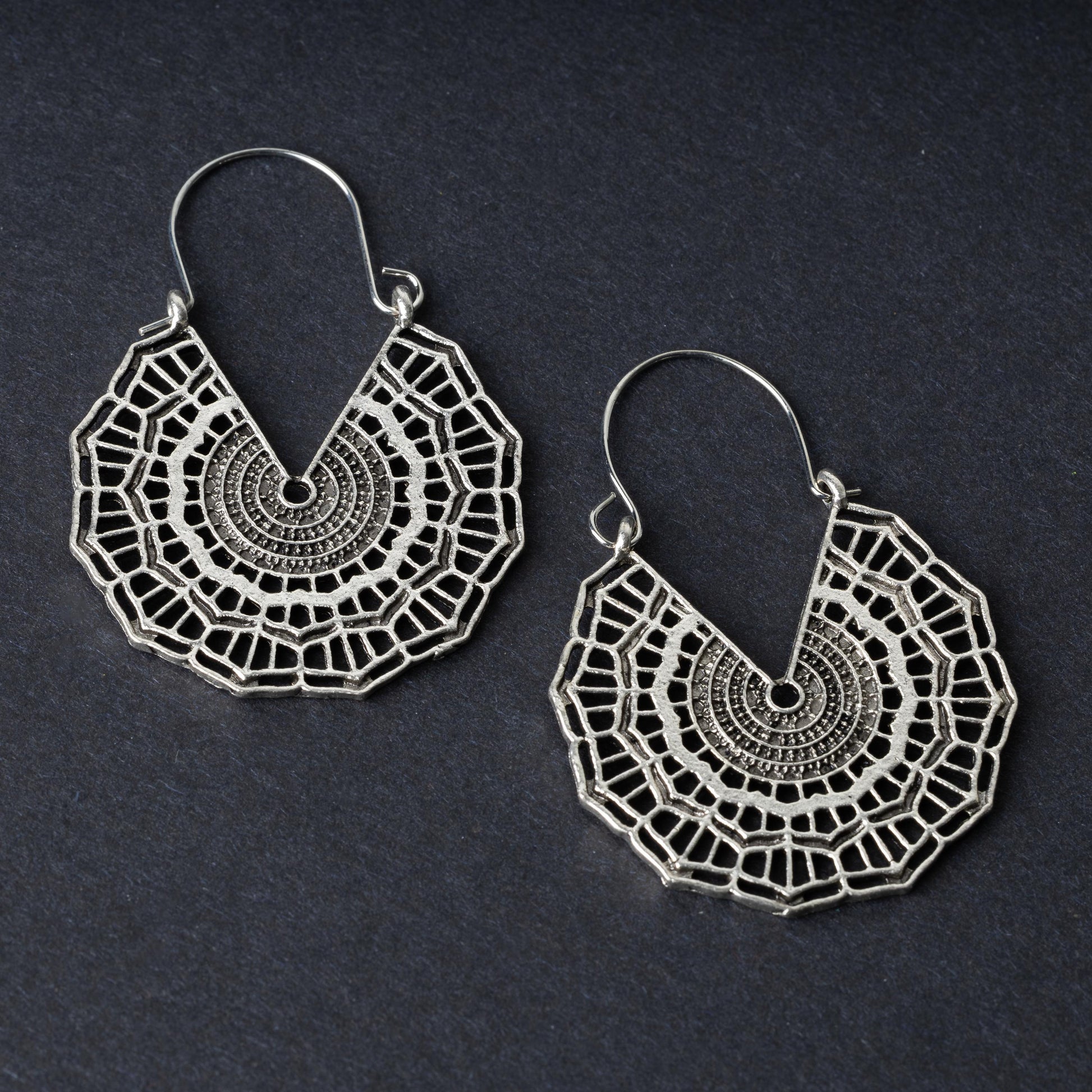 Mandala-inspired earrings in silver with intricate geometric designs, displayed on a dark background.