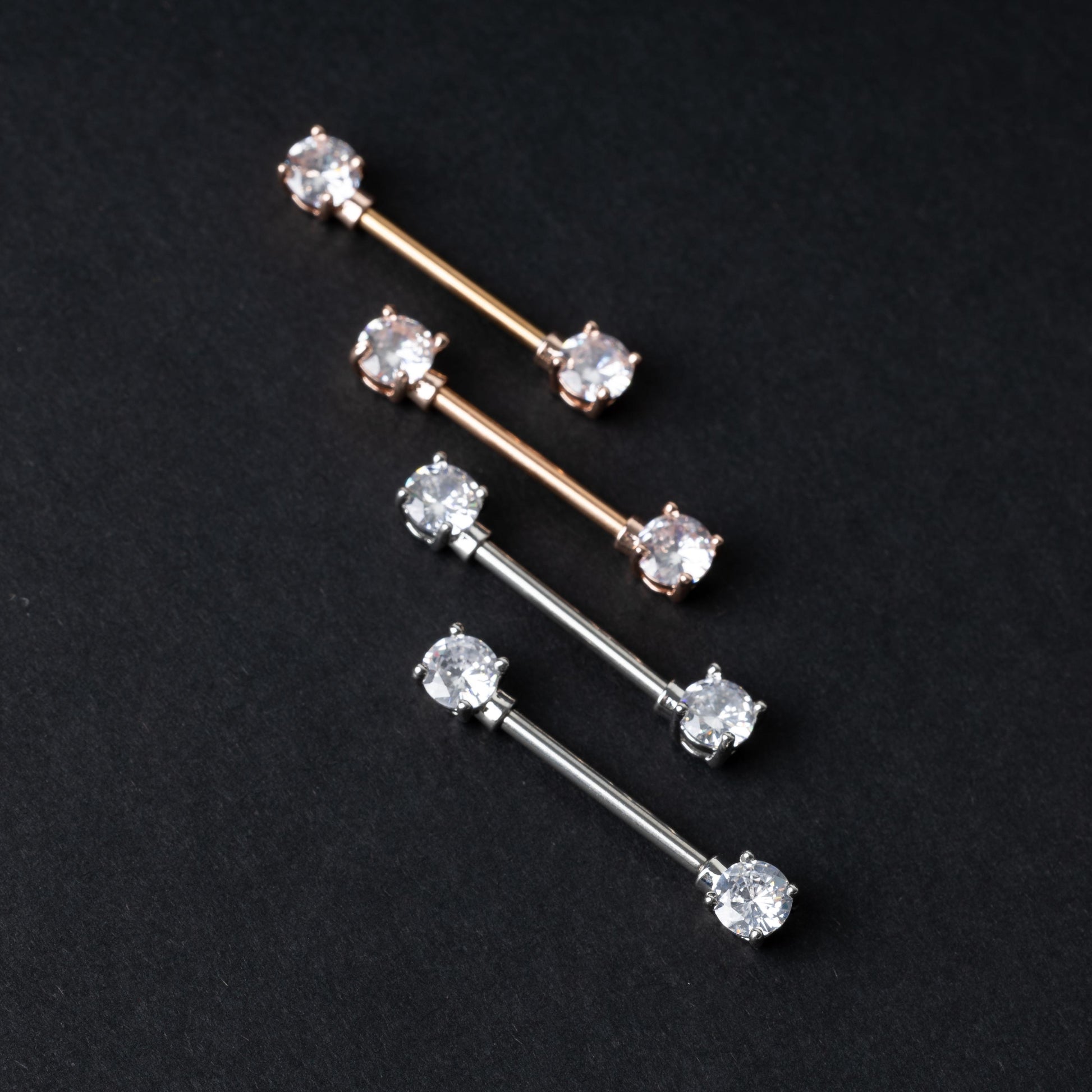 Four Crystal-studded barbells in rose gold and silver finishes, displayed on a dark background.