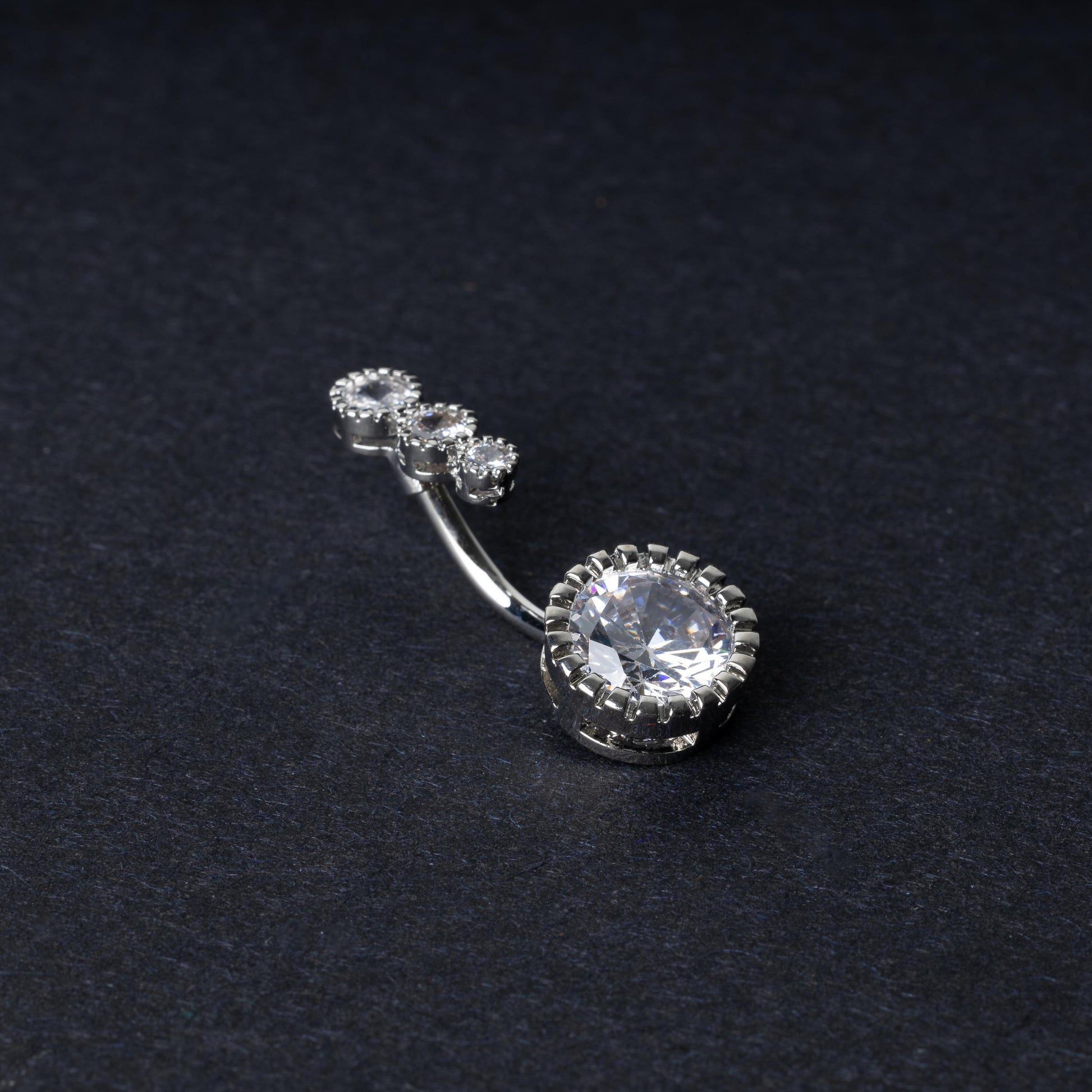 Double-jeweled belly rings in silver with large and small crystal accents, displayed on a dark background.