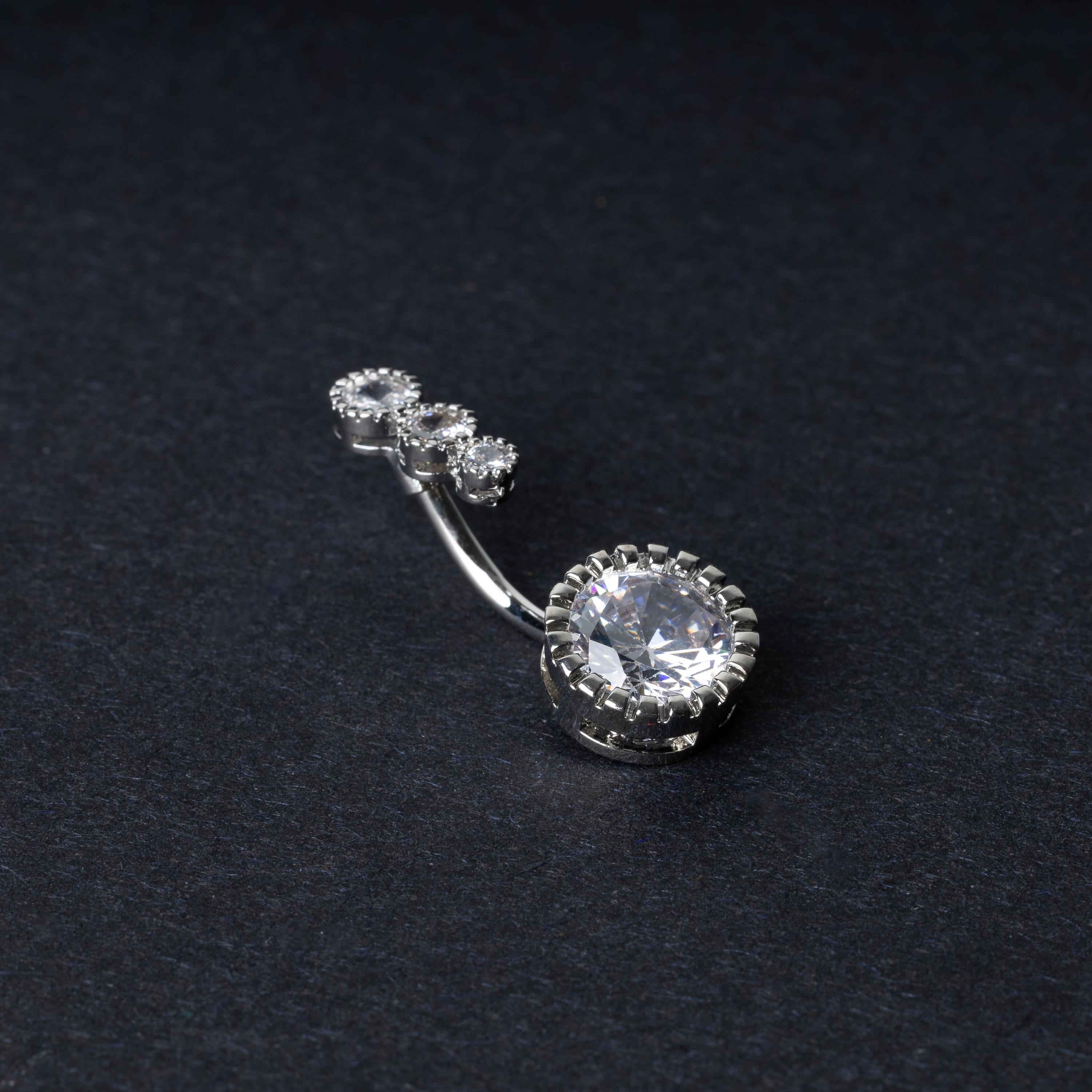 Double-jeweled belly rings in silver with large and small crystal accents, displayed on a dark background.