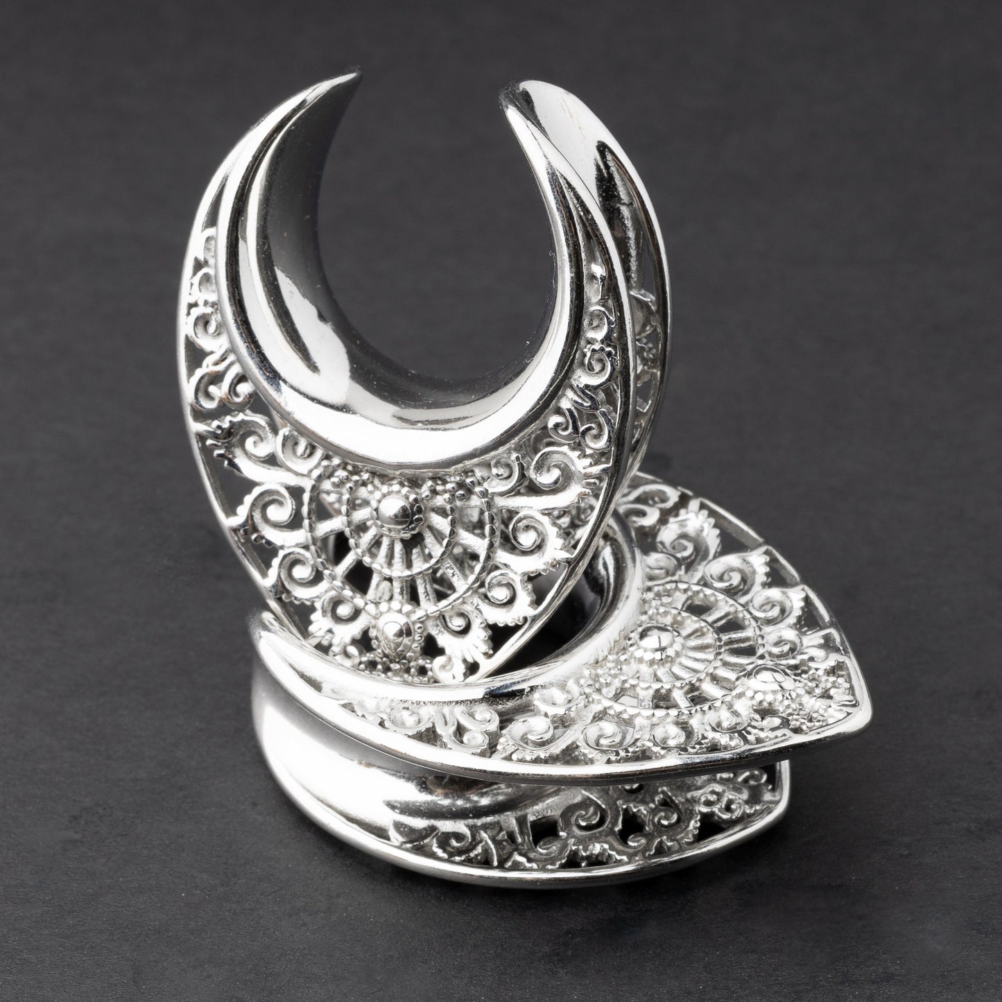 Crescent moon plugs for stretched ears in silver, displayed against a dark background.