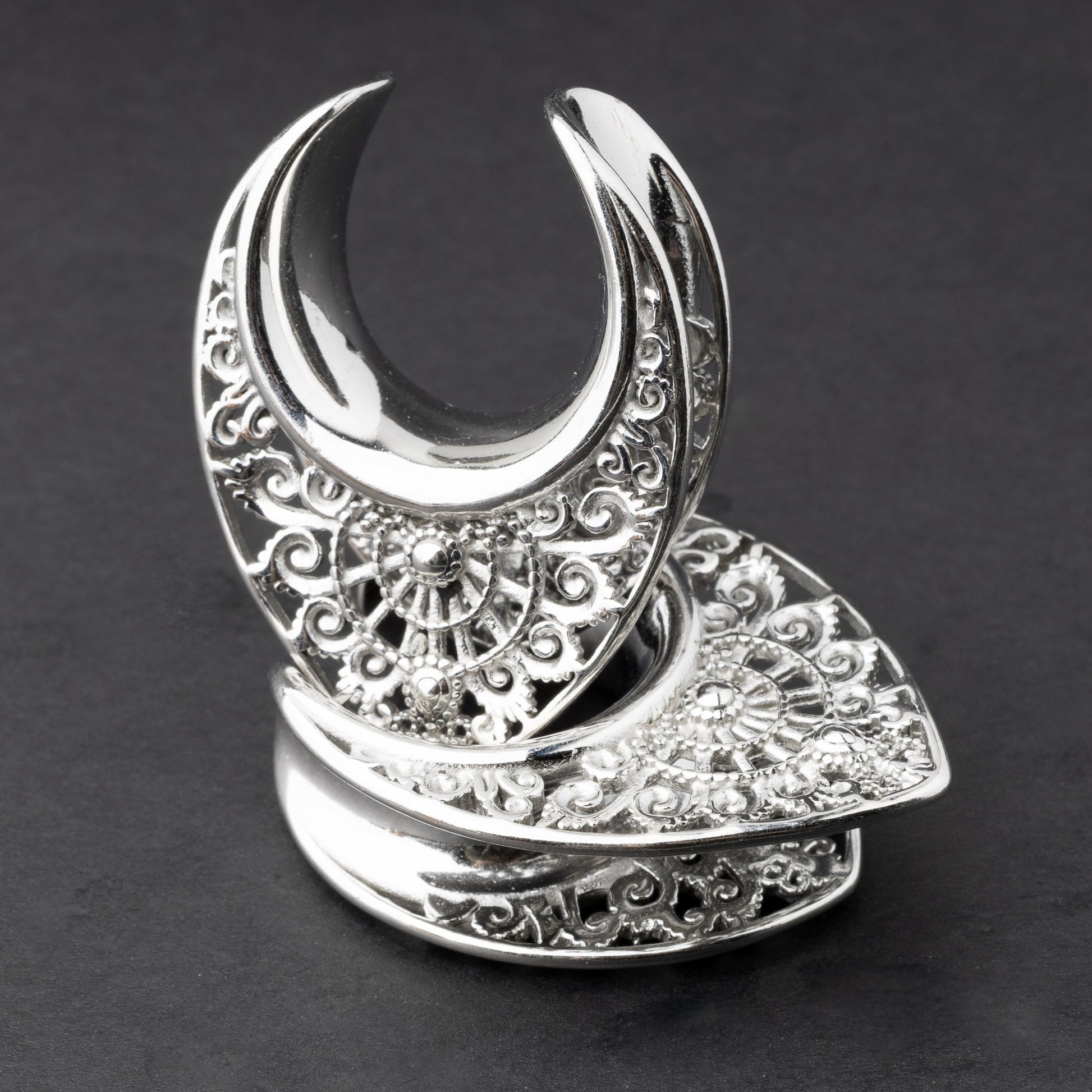 Crescent moon plugs for stretched ears in silver, displayed against a dark background.