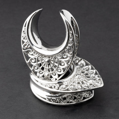 Crescent moon plugs for stretched ears in silver, displayed against a dark background.
