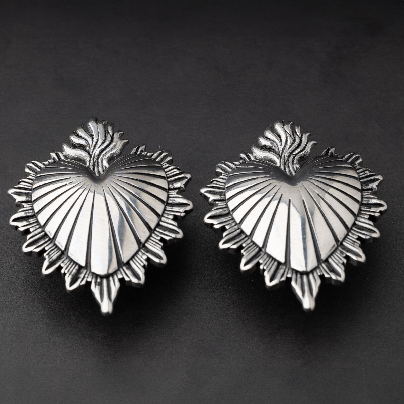 Sacred Heart-inspired plugs in silver, displayed on a matte dark background, showcasing intricate detailing and a bold design.