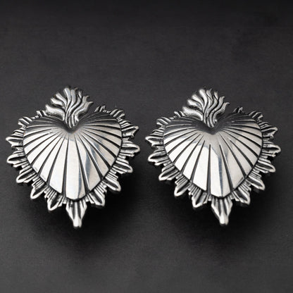 Sacred Heart-inspired plugs in silver, displayed on a matte dark background, showcasing intricate detailing and a bold design.