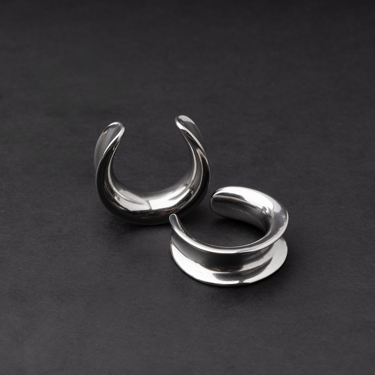 A pair of silver saddle tunnels displayed on a dark background.