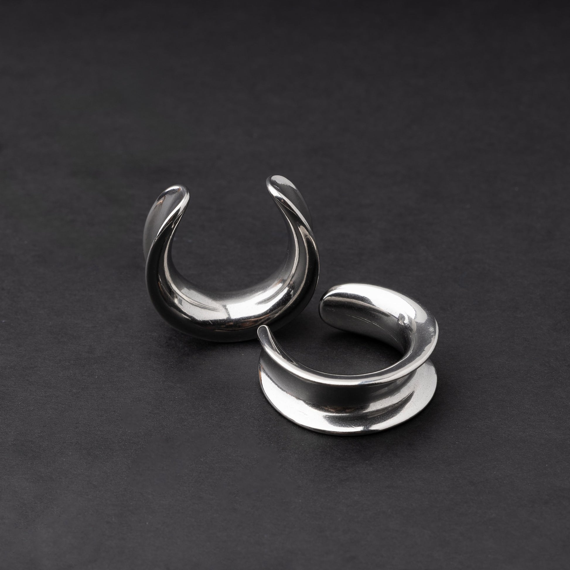 A pair of silver saddle tunnels displayed on a dark background.