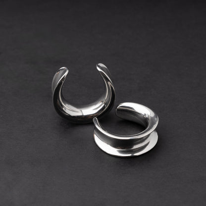 A pair of silver saddle tunnels displayed on a dark background.