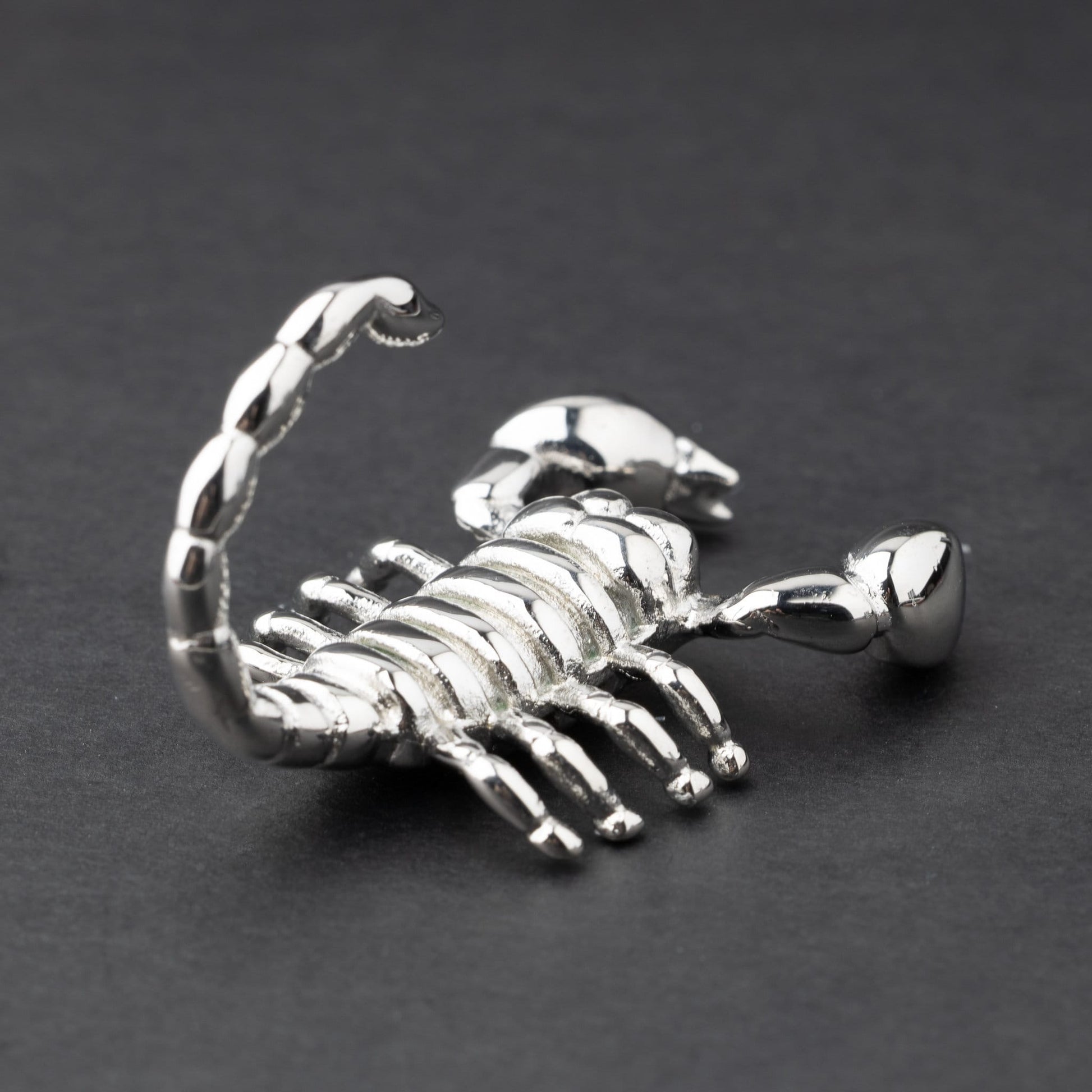 Scorpion-shaped ear hanger in silver and displayed on a dark matte background, highlighting their detailed and edgy design.