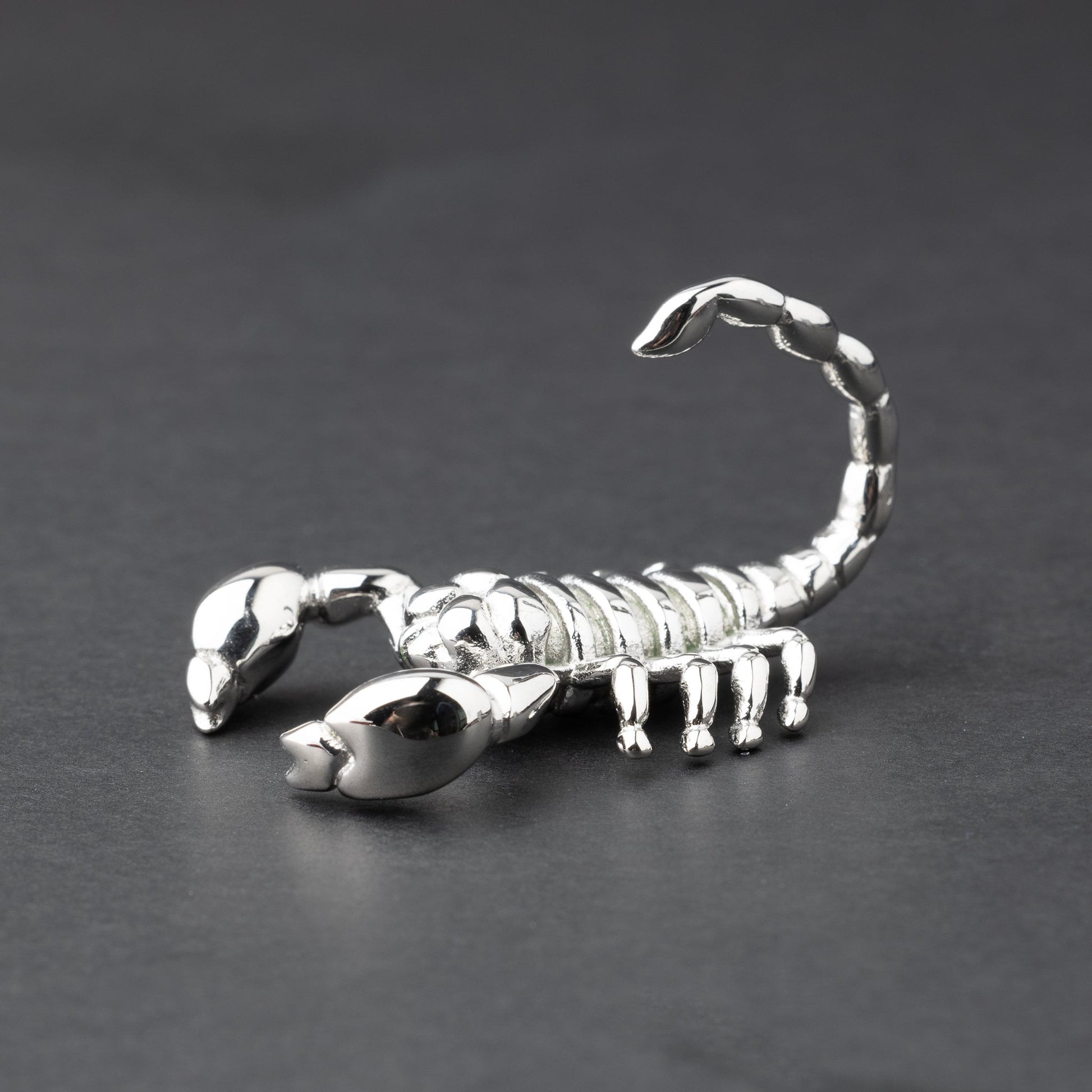 Scorpion-shaped ear hanger in silver and displayed on a dark matte background, highlighting their detailed and edgy design.