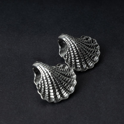 Two seashell-shaped ear weights in polished silver, with detailed textures and a bold design, displayed on a dark background.
