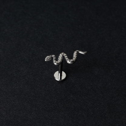 Silver-tone snake labret bars with intricate coiled snake designs displayed on a dark background.

