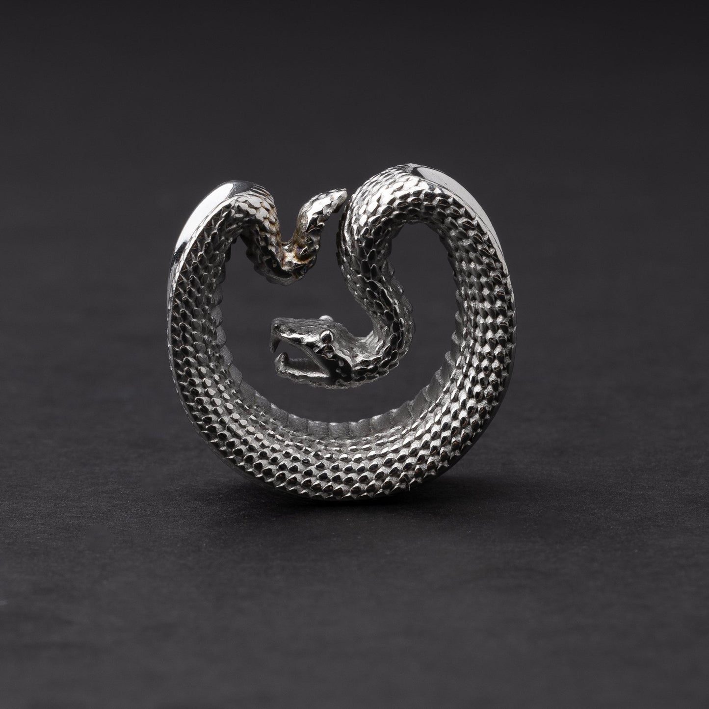 Silver Snake-shaped saddle plugs, displayed on a dark background.