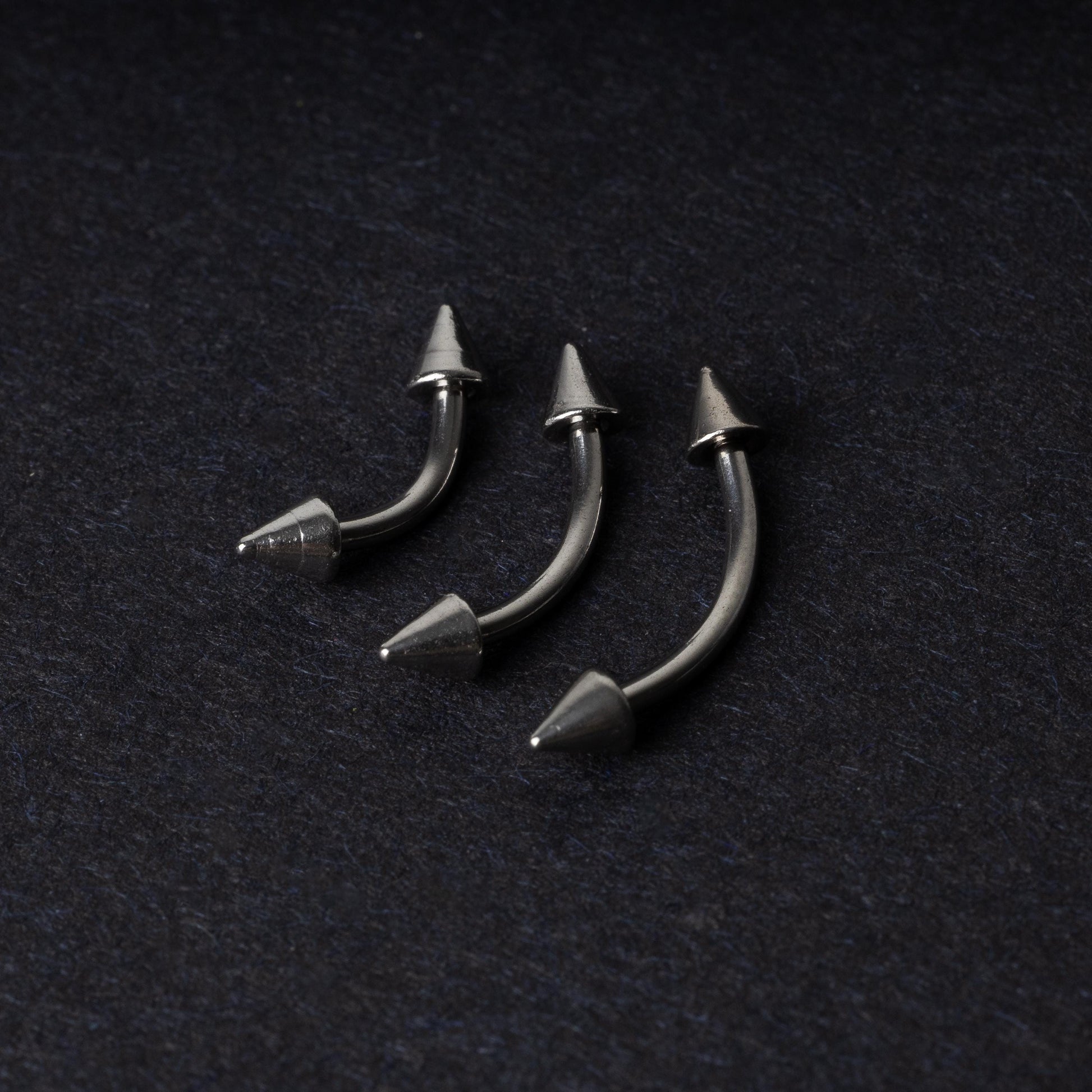 Three stainless steel curved barbells with cone-shaped ends, displayed on a dark background.