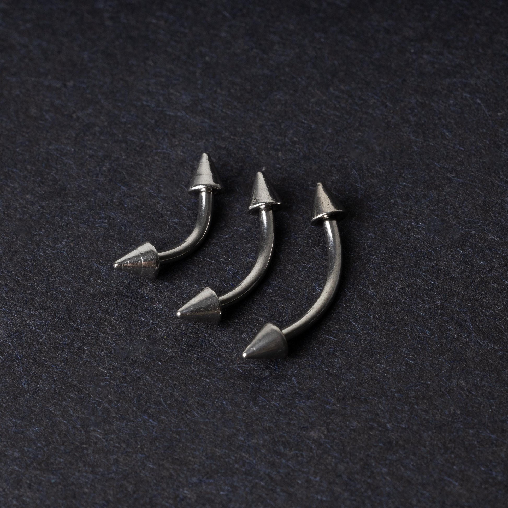 Three stainless steel curved barbells with cone-shaped ends, displayed on a dark background.
