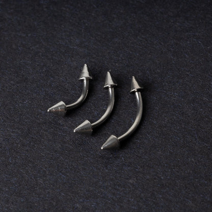 Three stainless steel curved barbells with cone-shaped ends, displayed on a dark background.