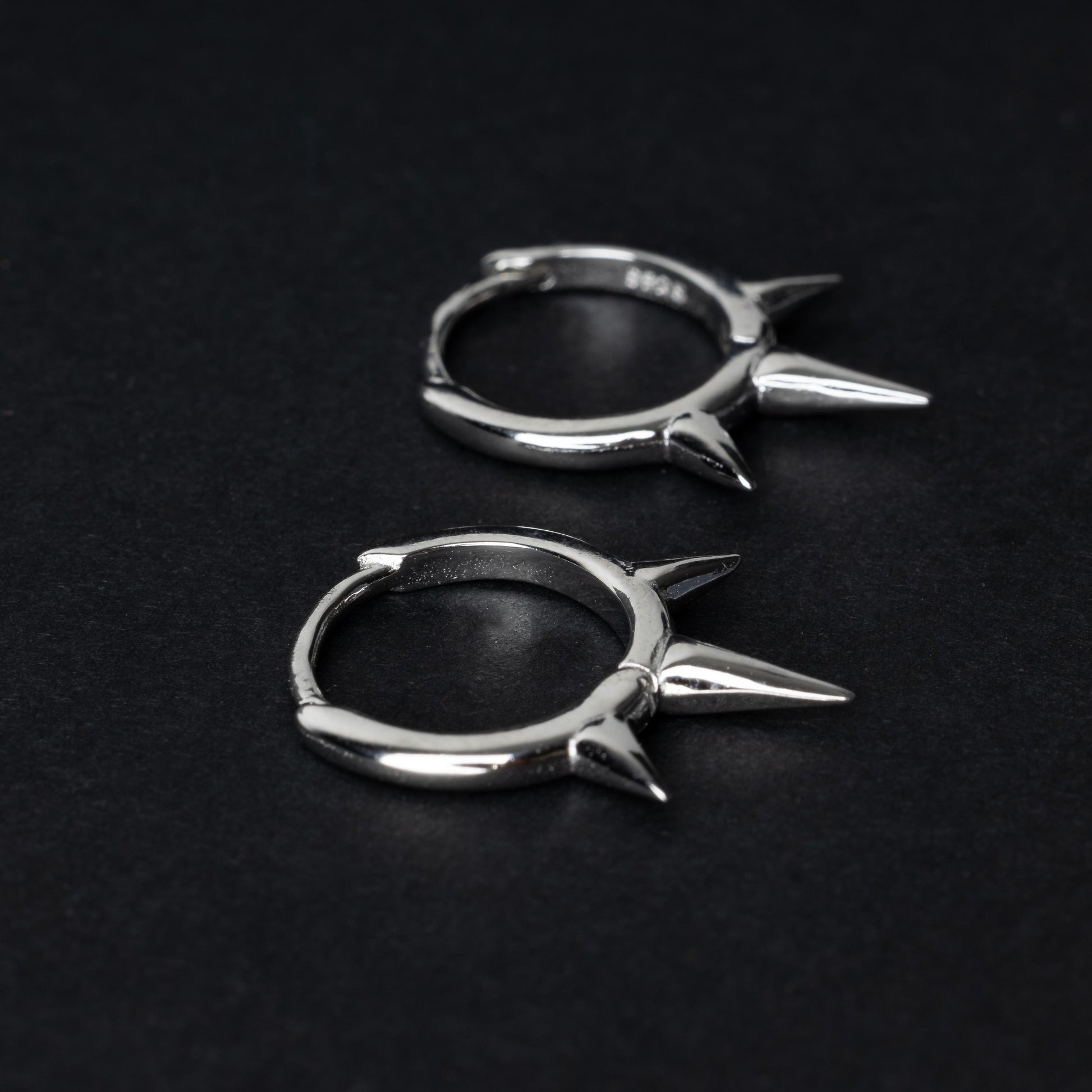 Pair of sterling silver spiked clicker rings with three evenly spaced spikes, displayed on a dark textured background.