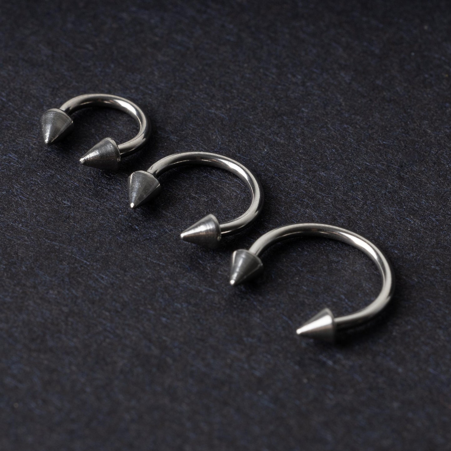 Three stainless steel horseshoe hoops with cone-shaped ends, arranged on a dark background.
