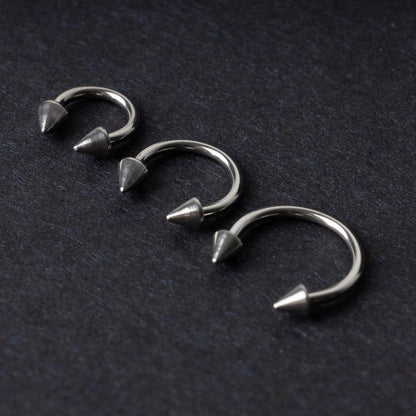 Three stainless steel horseshoe hoops with cone-shaped ends, arranged on a dark background.