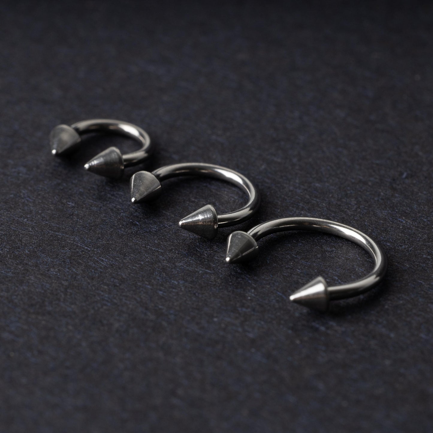 Three stainless steel horseshoe hoops with cone-shaped ends, arranged on a dark background.