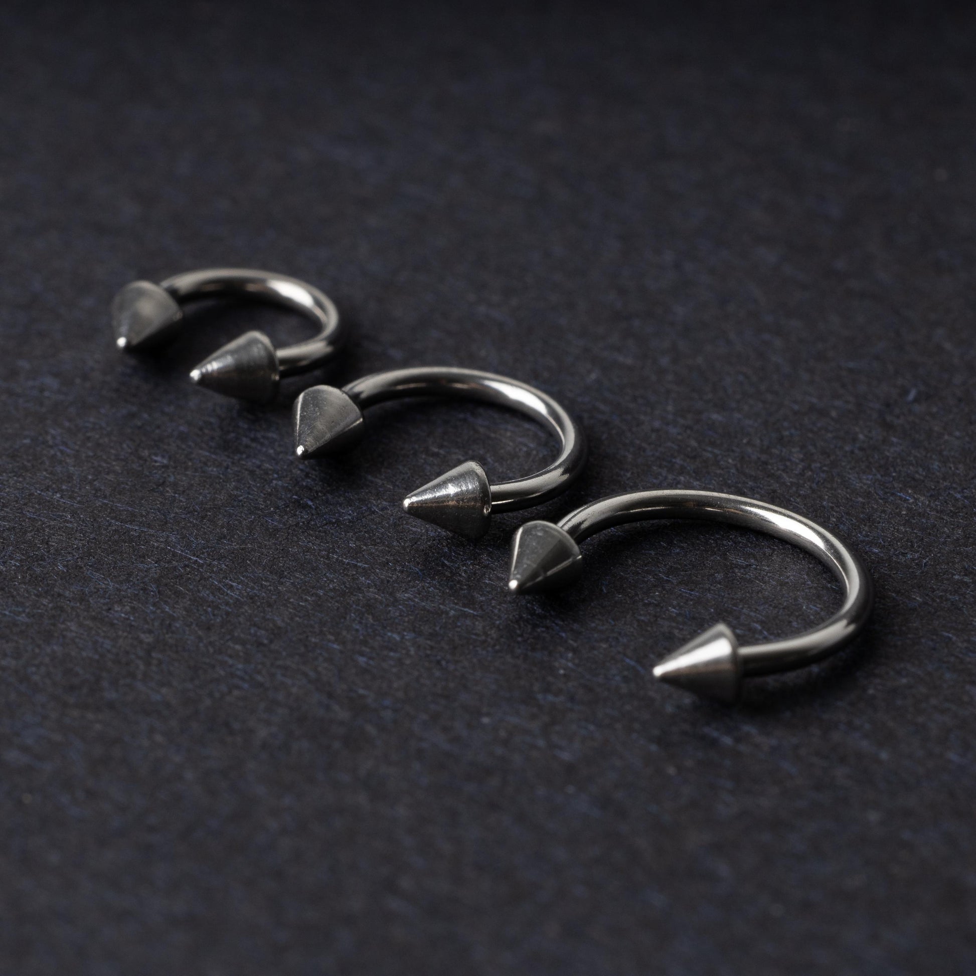 Three stainless steel horseshoe hoops with cone-shaped ends, arranged on a dark background.