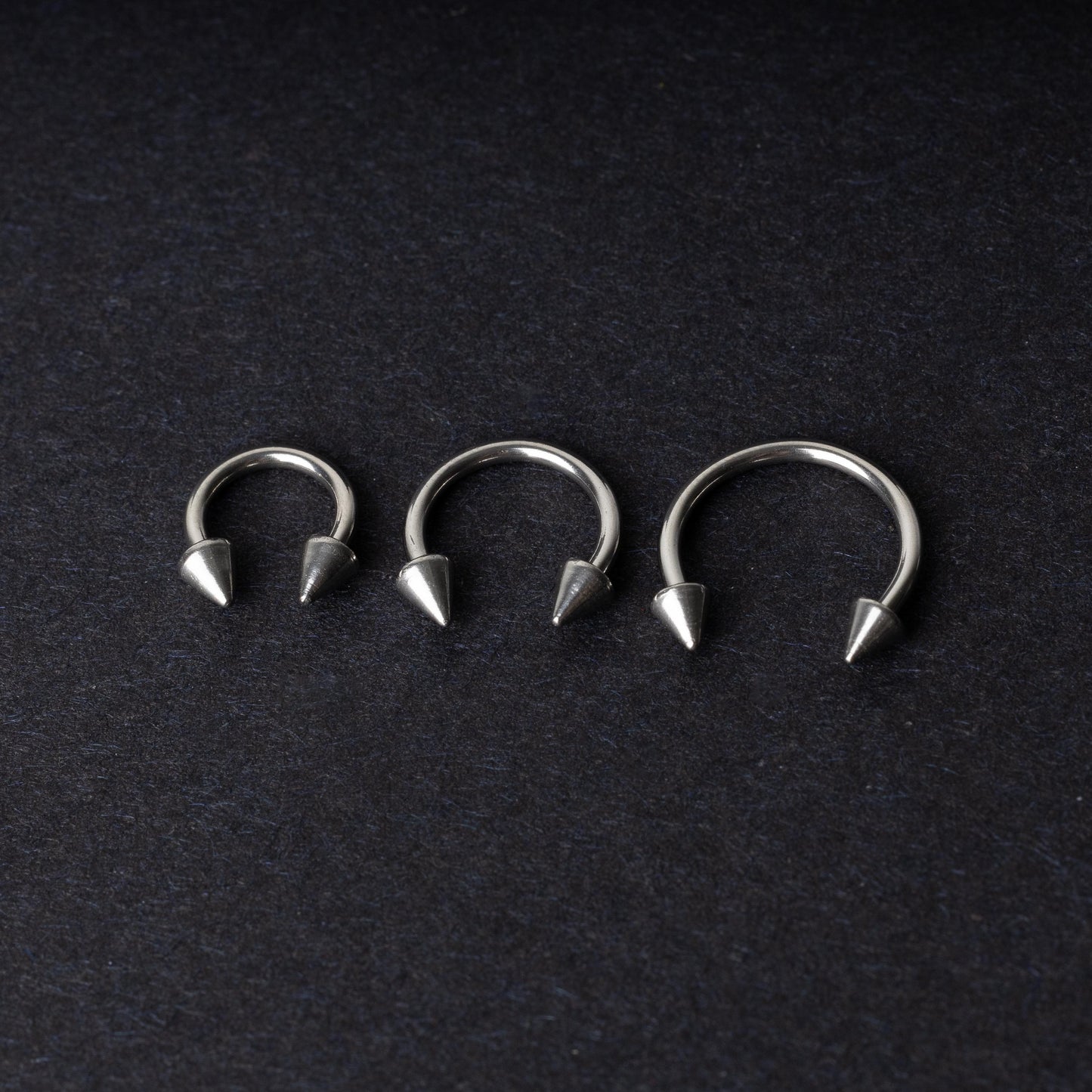 Three stainless steel horseshoe hoops with cone-shaped ends, arranged on a dark background.