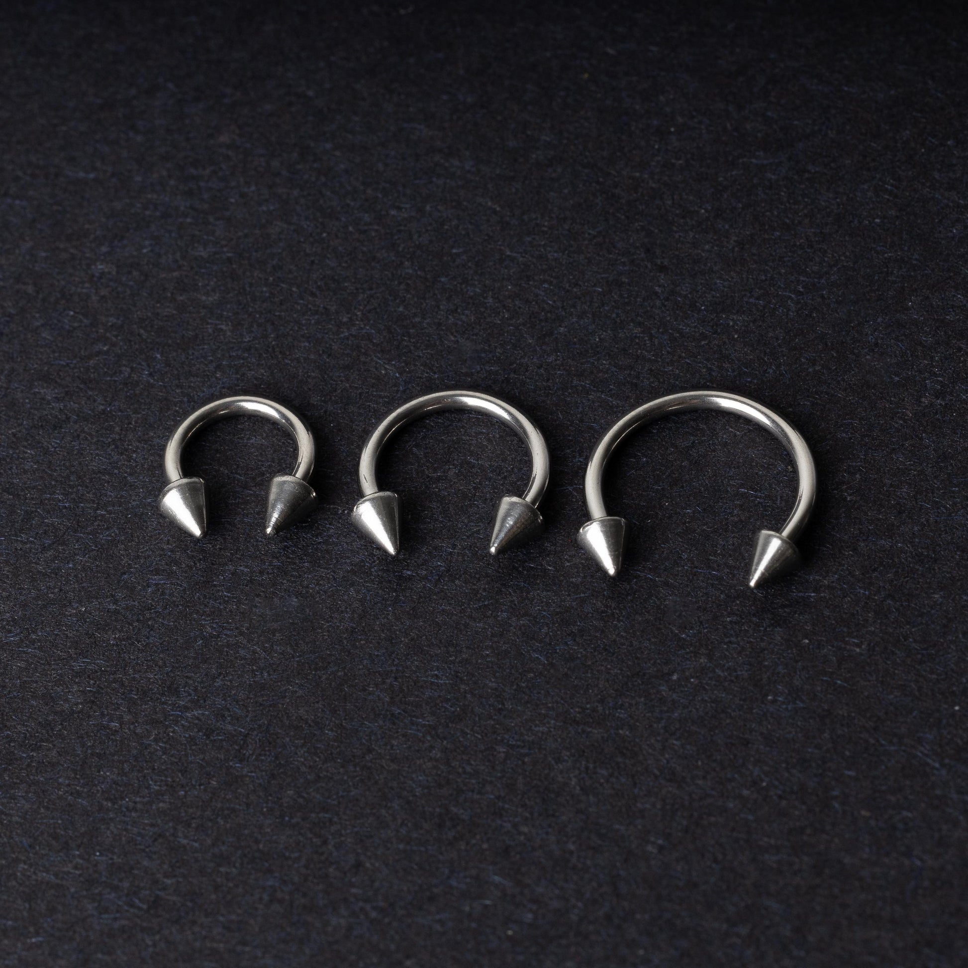 Three stainless steel horseshoe hoops with cone-shaped ends, arranged on a dark background.