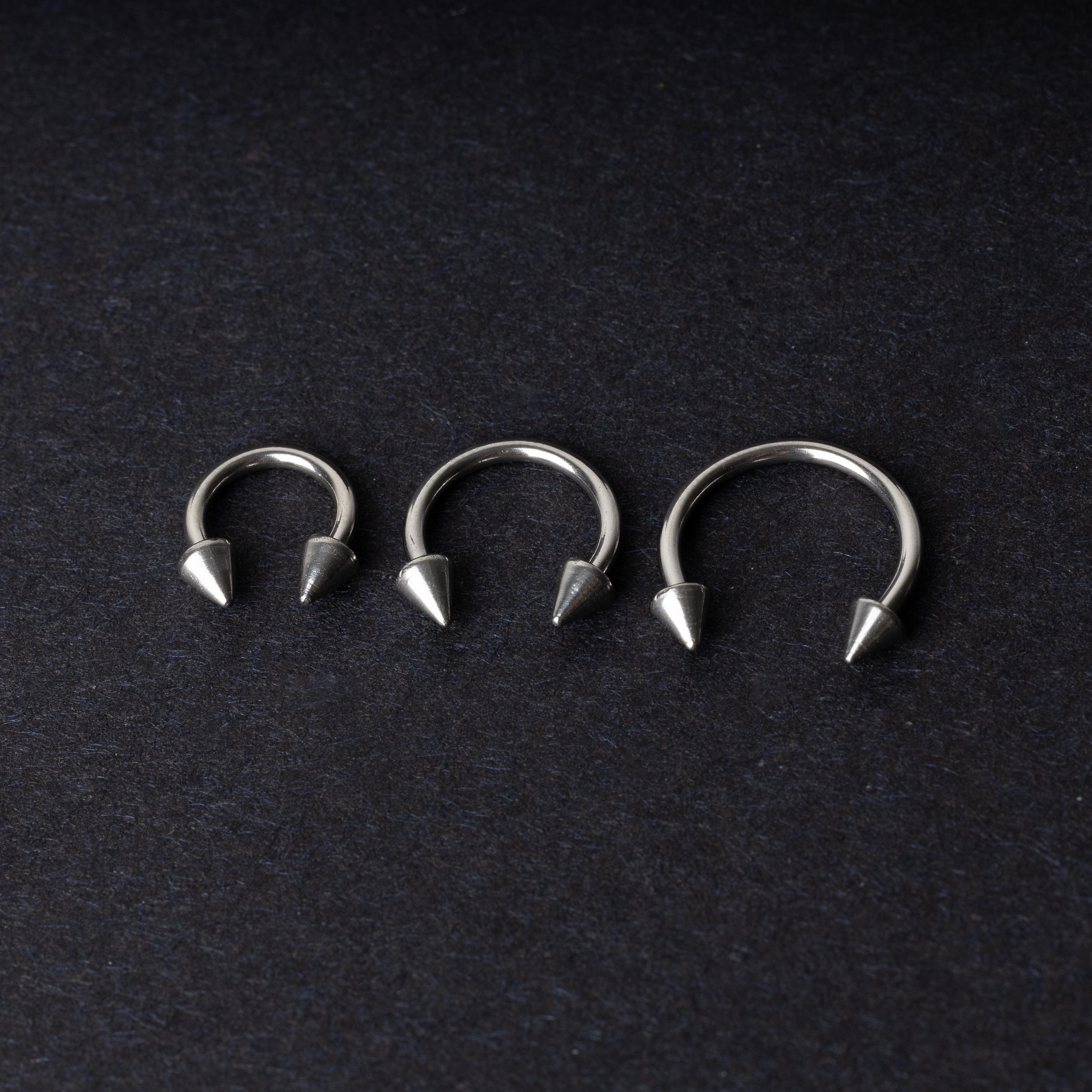 Three stainless steel horseshoe hoops with cone-shaped ends, arranged on a dark background.