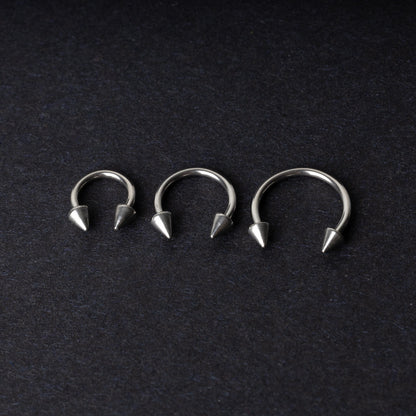 Three stainless steel horseshoe hoops with cone-shaped ends, arranged on a dark background.