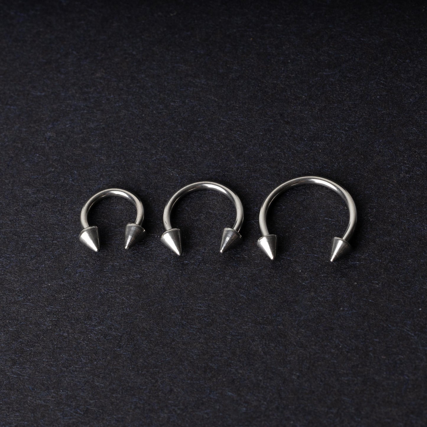 Three stainless steel horseshoe hoops with cone-shaped ends, arranged on a dark background.