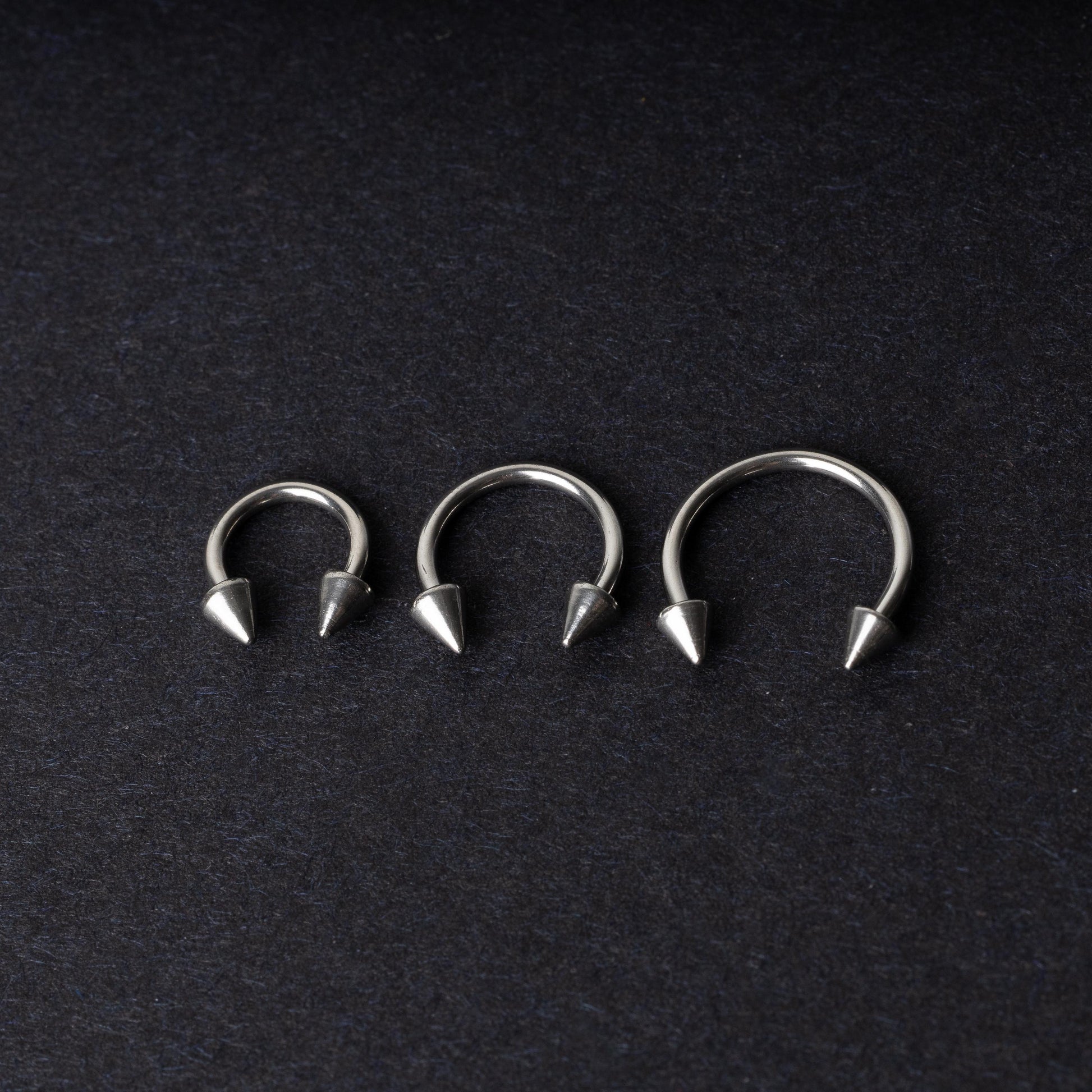 Three stainless steel horseshoe hoops with cone-shaped ends, arranged on a dark background.