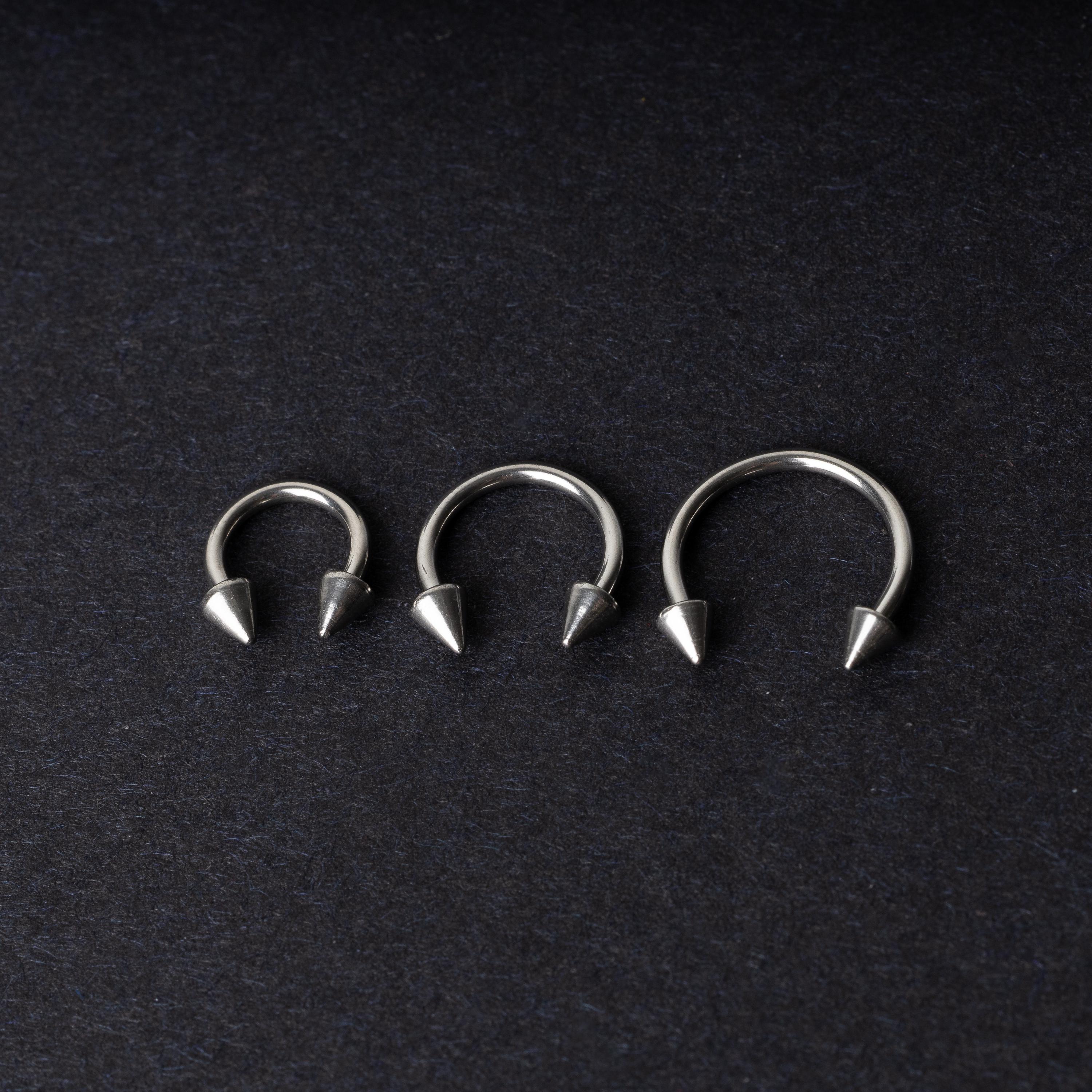 Three stainless steel horseshoe hoops with cone-shaped ends, arranged on a dark background.