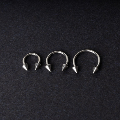 Three stainless steel horseshoe hoops with cone-shaped ends, arranged on a dark background.