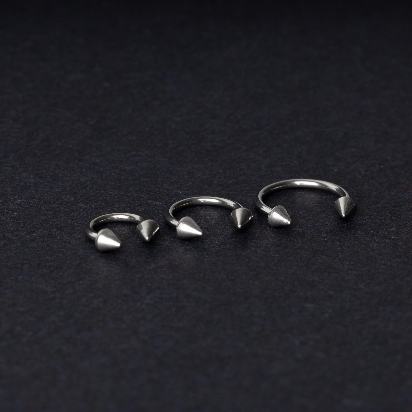 Three stainless steel horseshoe hoops with cone-shaped ends, arranged on a dark background.