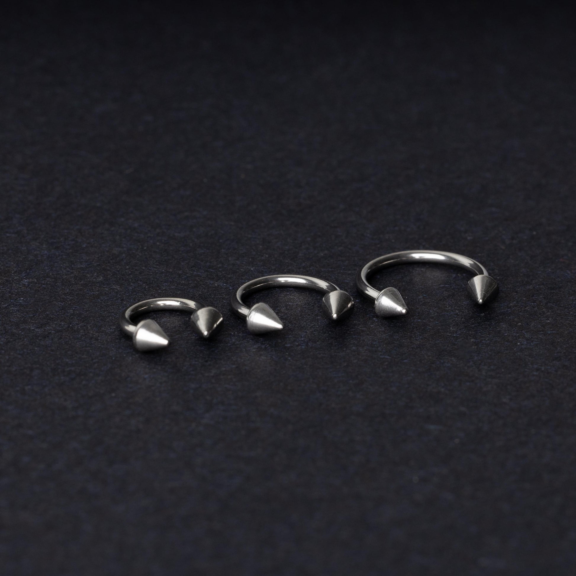 Three stainless steel horseshoe hoops with cone-shaped ends, arranged on a dark background.