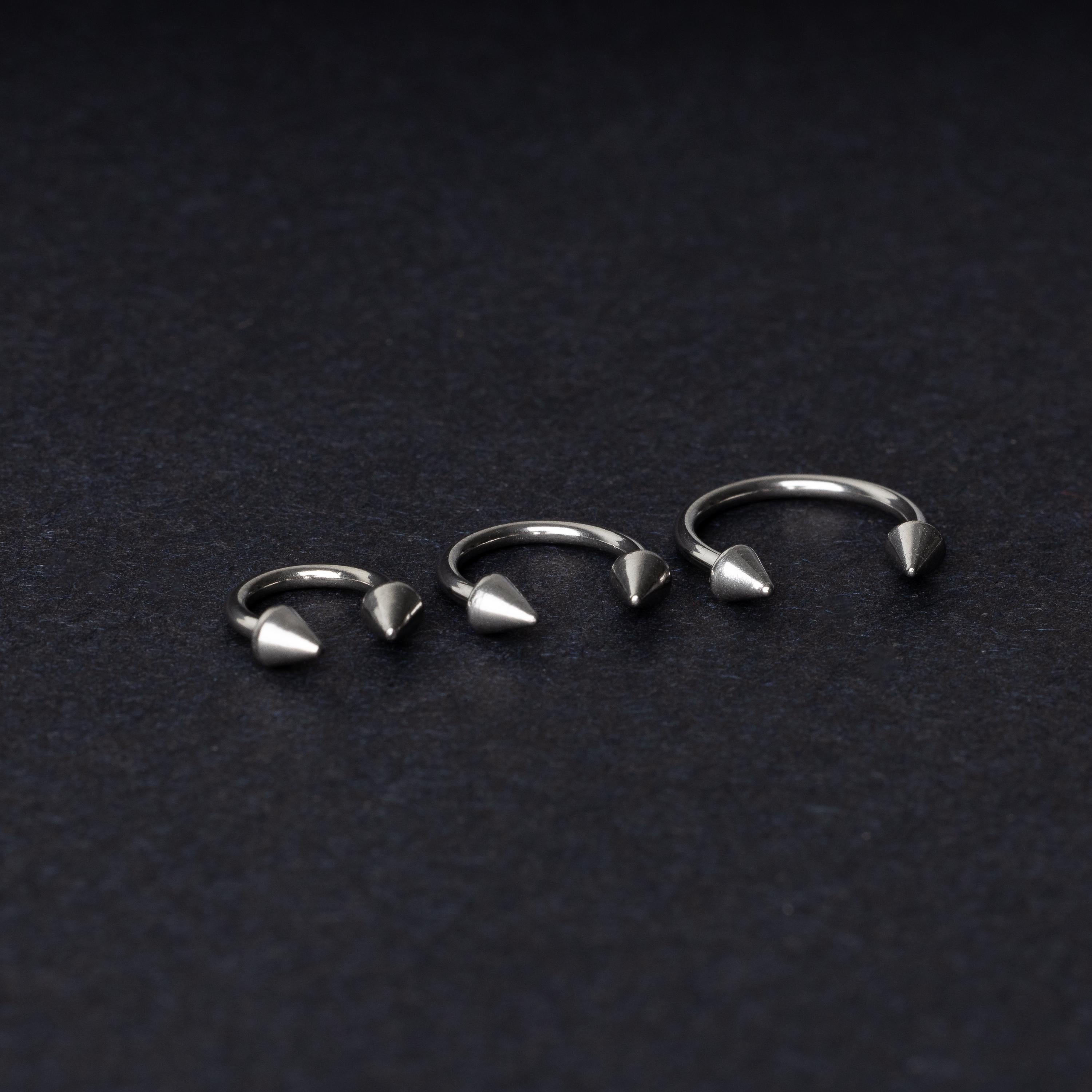 Three stainless steel horseshoe hoops with cone-shaped ends, arranged on a dark background.