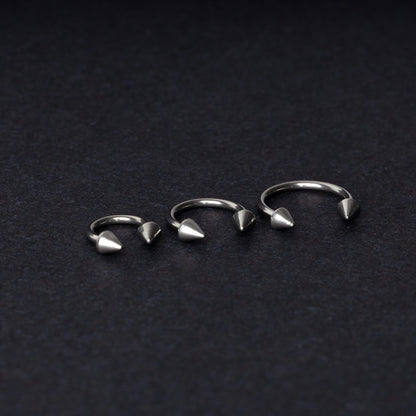 Three stainless steel horseshoe hoops with cone-shaped ends, arranged on a dark background.