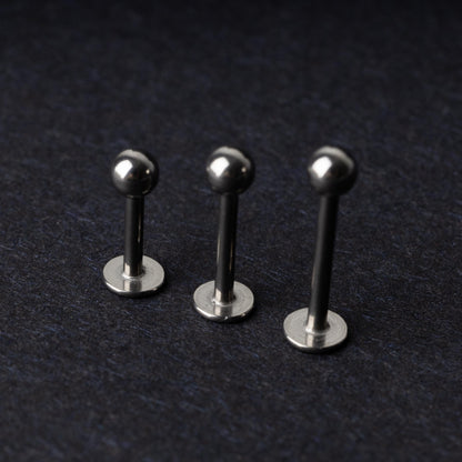Three silver stainless steel labret studs with flat backs and polished ball ends, displayed on a dark textured background.