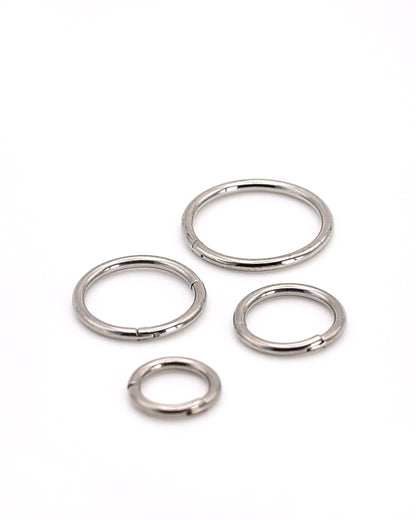 A selection of silver coloured titanium clicker hoops on a white background. 
