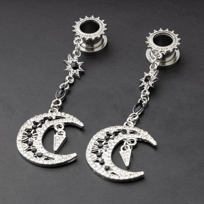 A pair of silver ear hangers for stretched ears with dangling crescent moon and star designs, adorned with black and clear rhinestones, displayed on a dark background.